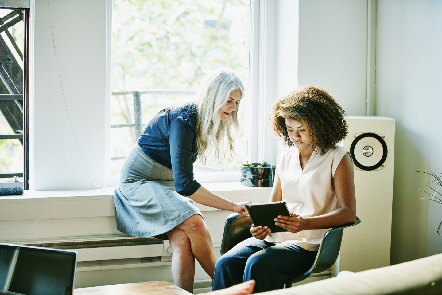 Mature businesswoman assists younger worker with project.