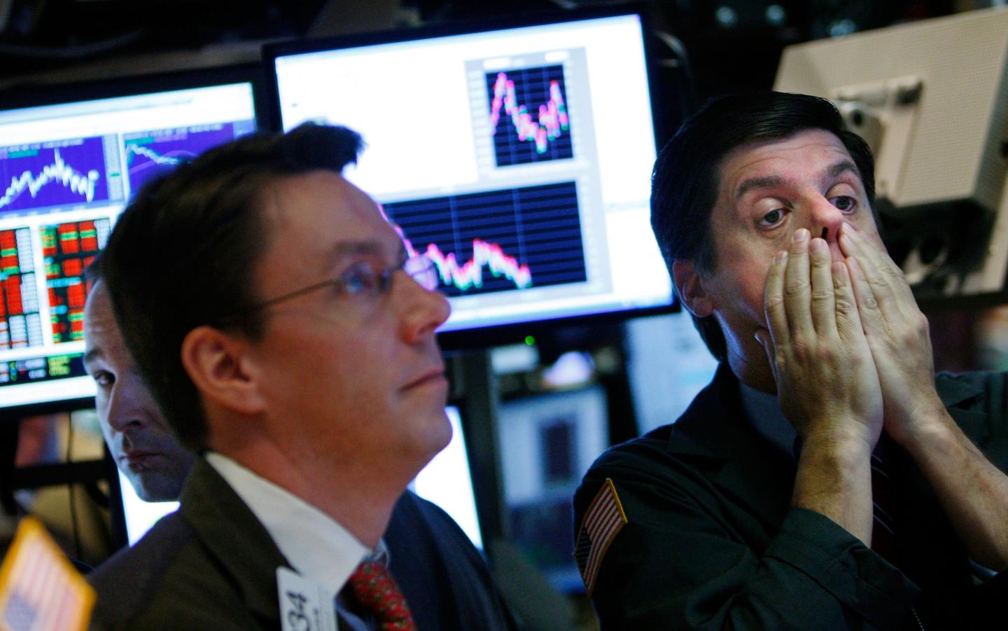 A trader rubs his face looking anxious while working on the floor of the New York Stock Exchange