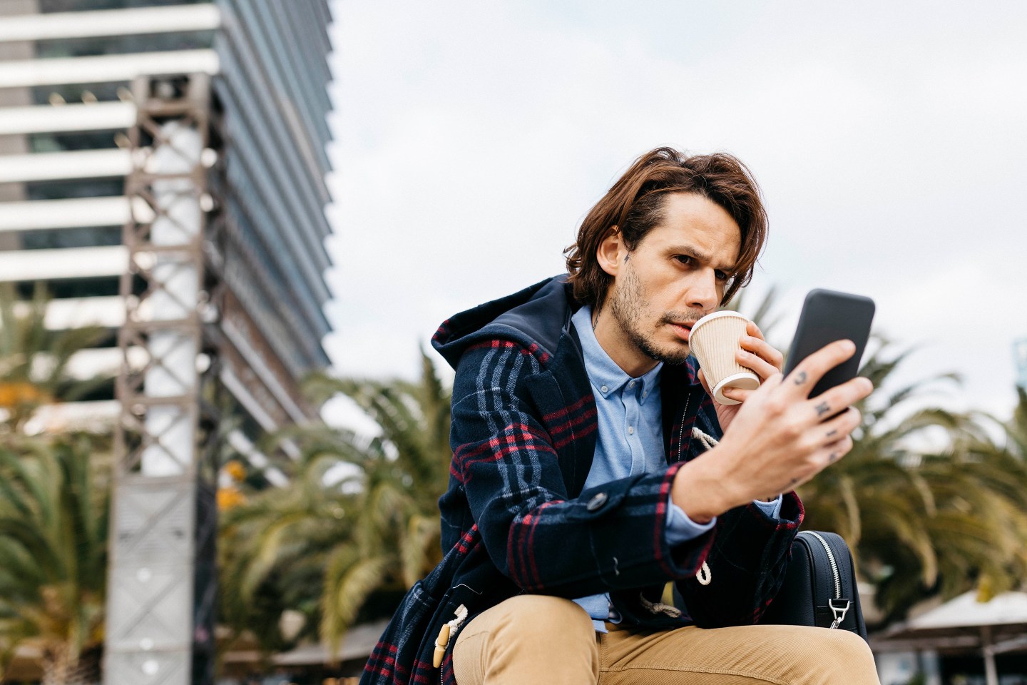 Man watches news on phone while drinking coffee.