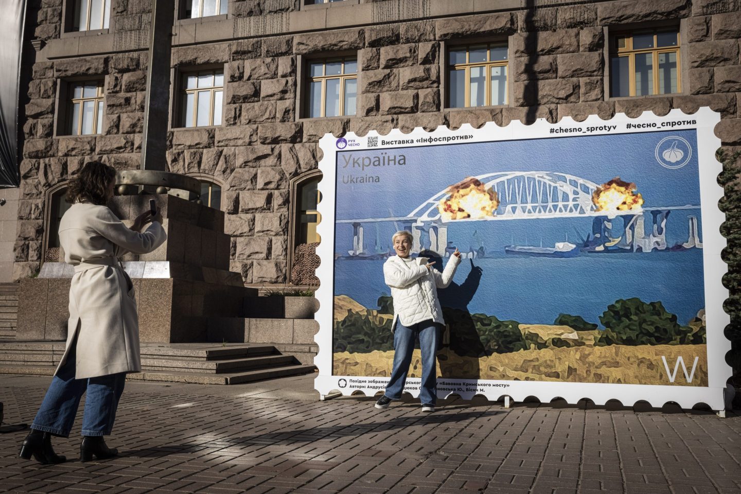 People pose in front of a picture of a postage stamp showing an artist's impression of the Kerch bridge explosion on Saturday in central Kyiv.
