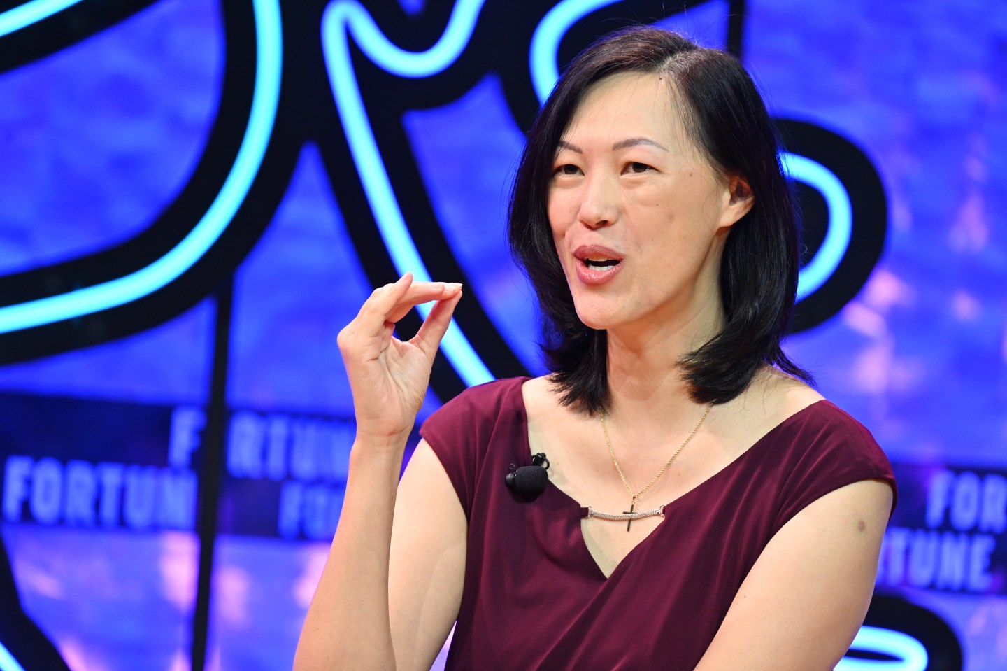 Deb Liu CEO of Ancestry on stage talking with her hands in front of a purple and blue background.
