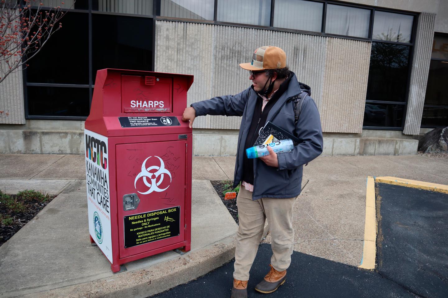A man stands in front of a syringe disposal box.