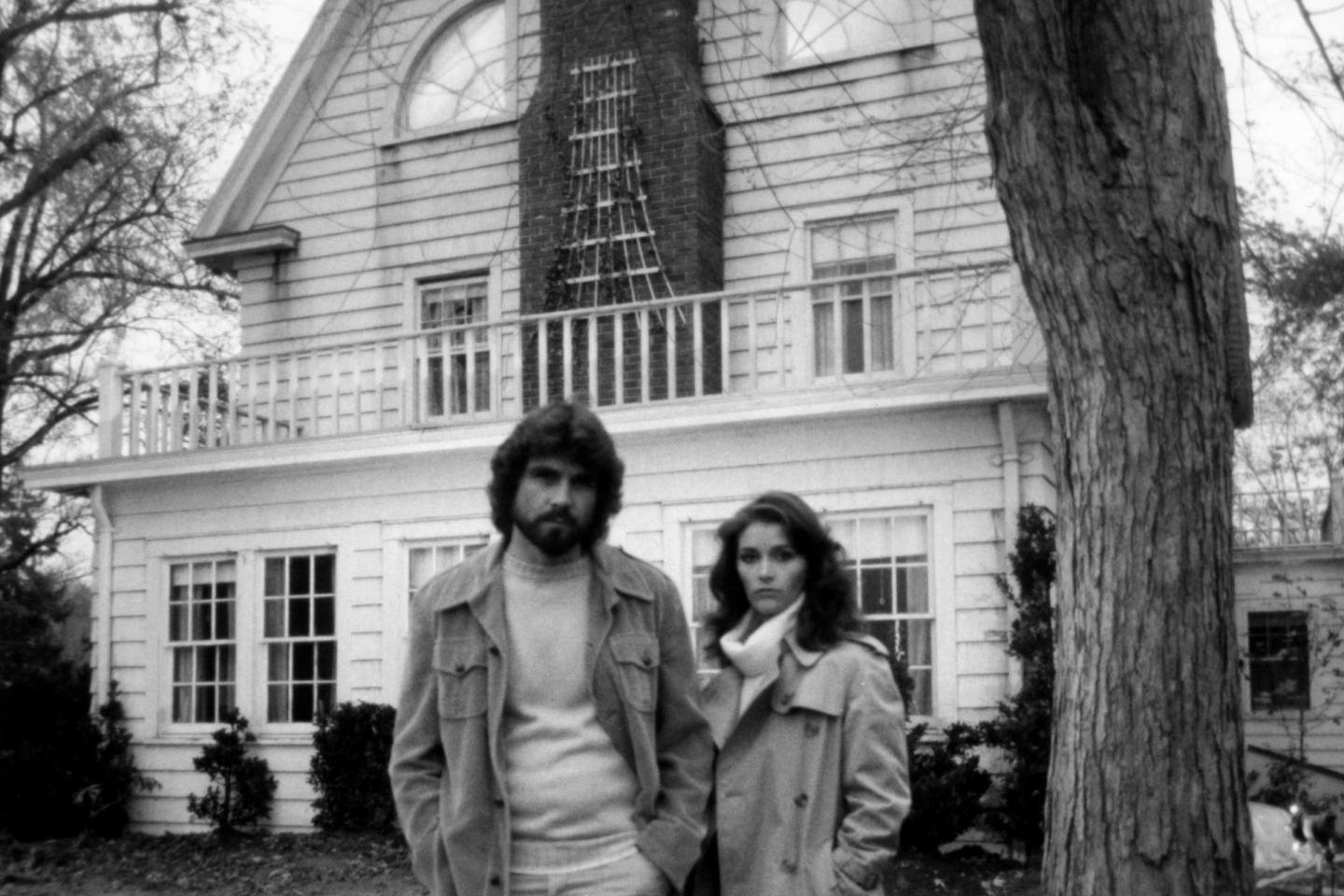 James Brolin and Margot Kidder posing in front of a house in a scene from film 'The Amityville Horror', 1979.