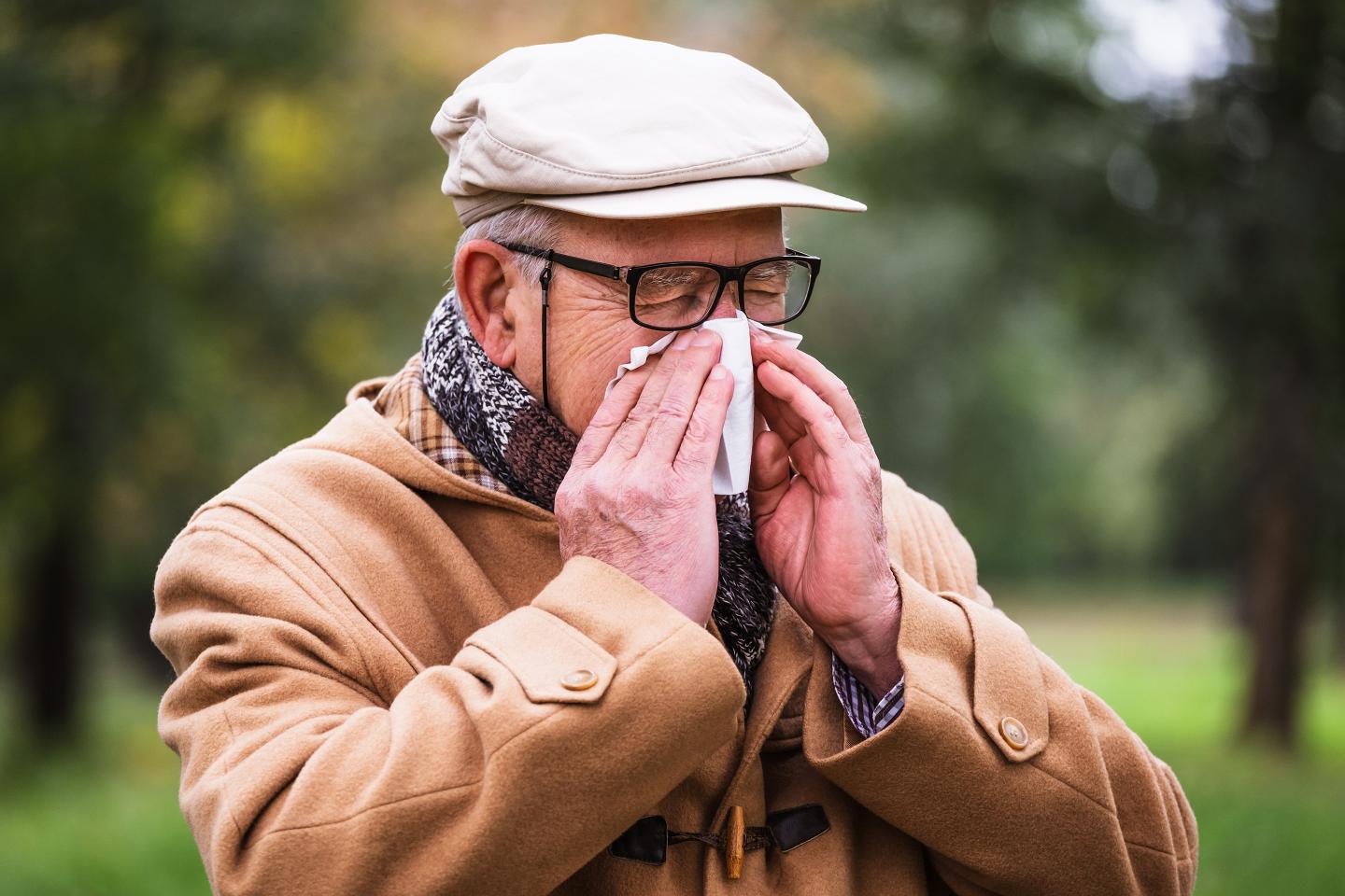 Outdoor portrait of senior man who is blowing nose in winter time in park.