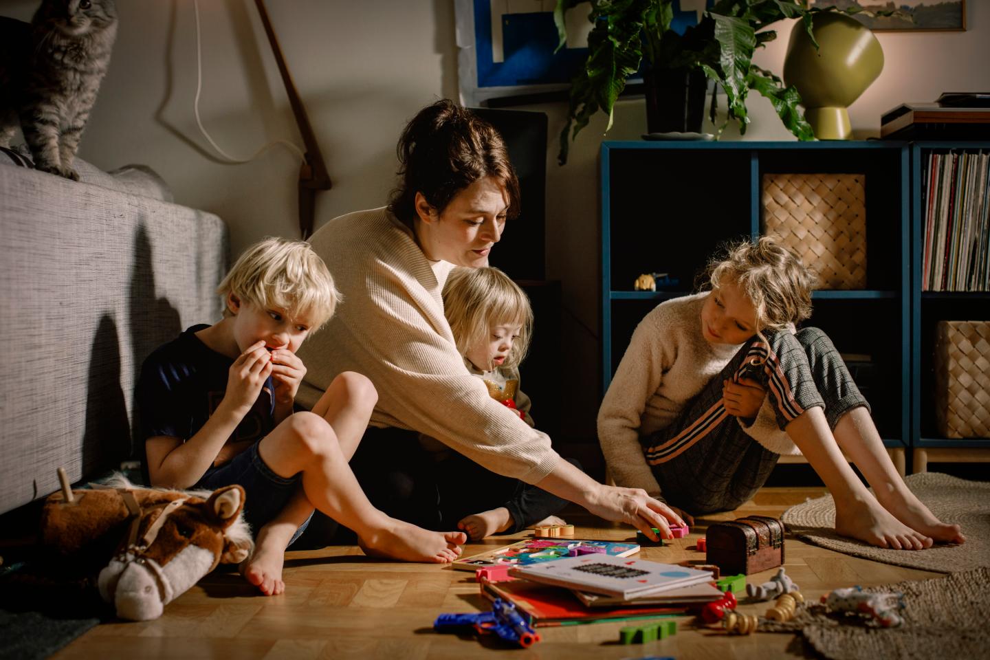 A mother plays with her three children as they all sit on the floor of their home together.