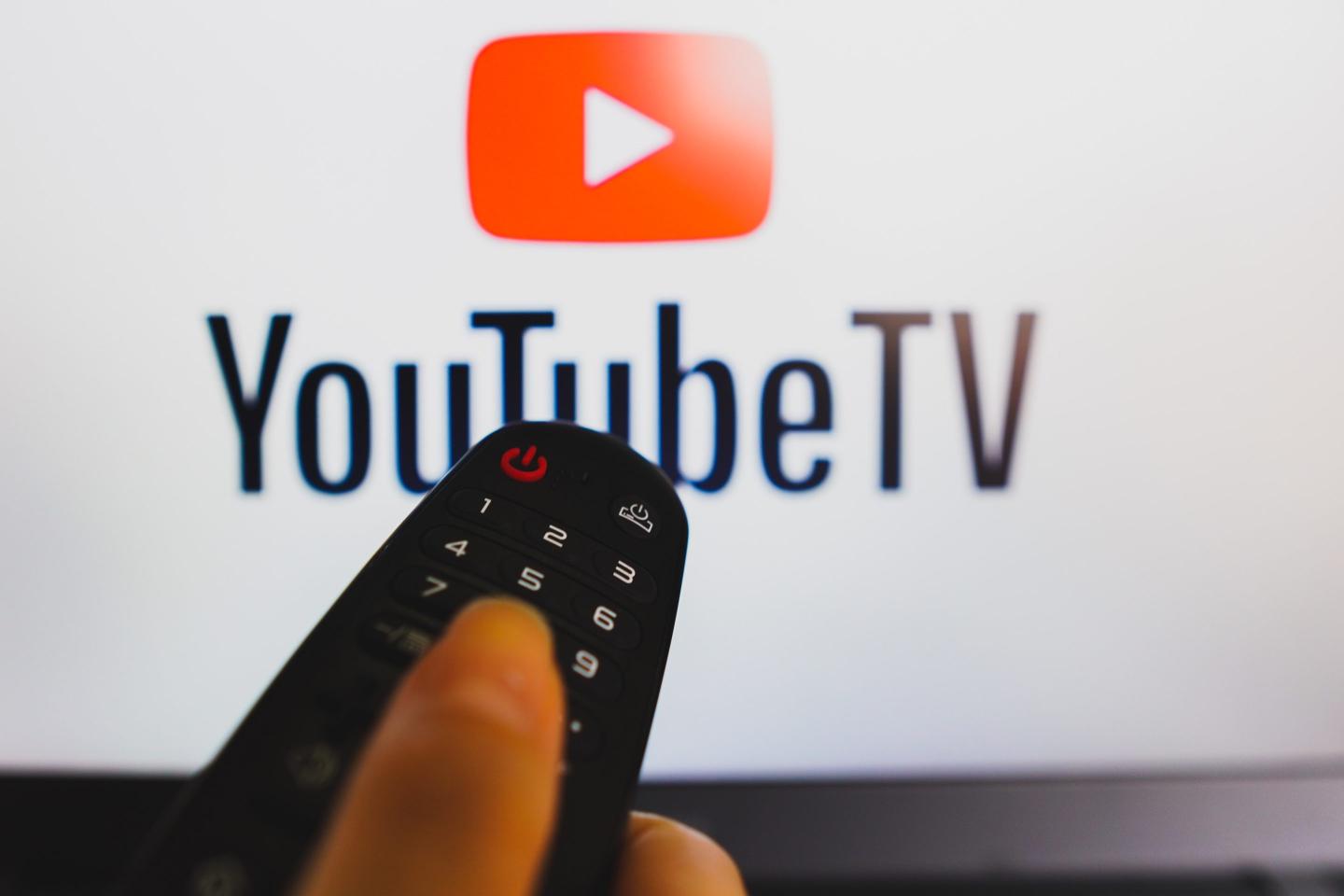 A hand holding a TV remote control in front of a YouTube logo on a TV screen.