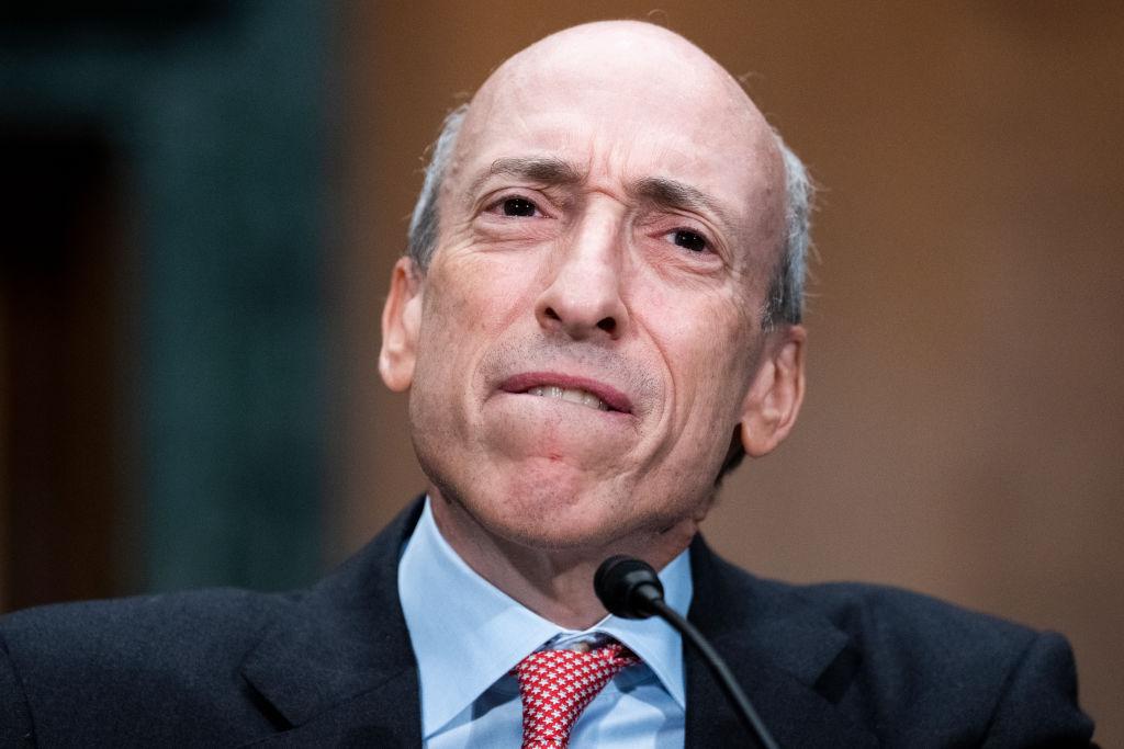A white man with a blue shirt and orange tie speaks into a microphone