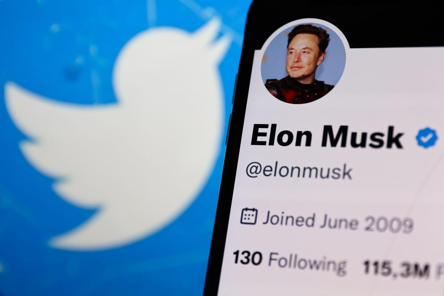 Elon Musk account on Twitter displayed on a phone screen and Twitter logo displayed on a laptop screen