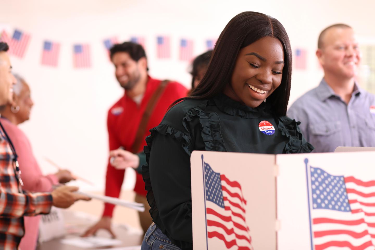 A Black women stands in front of a voting booth.