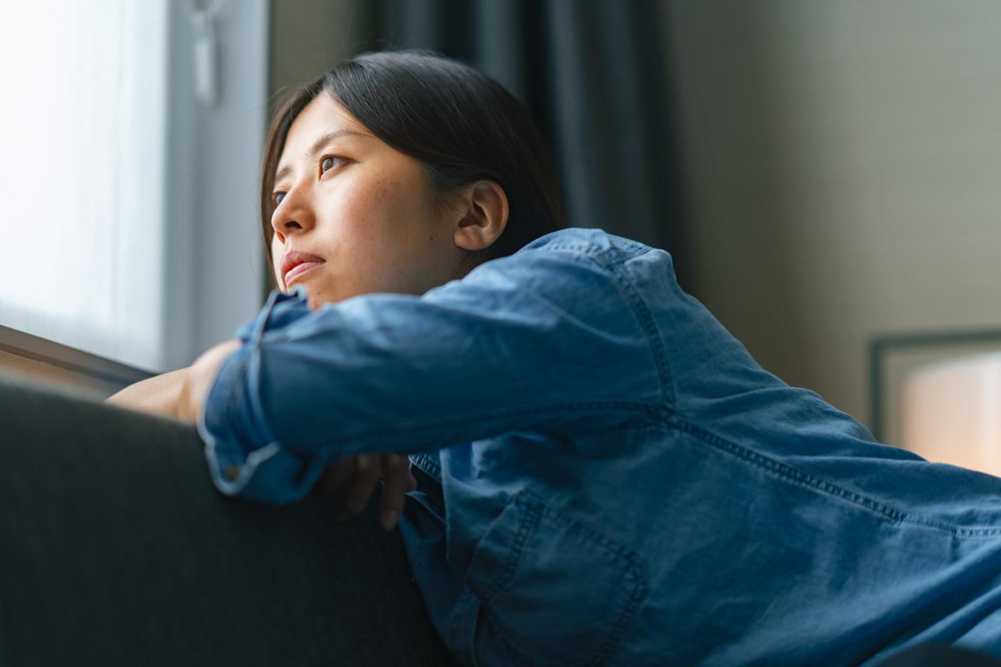 Young woman sitting on sofa by window and looking outside through window at home