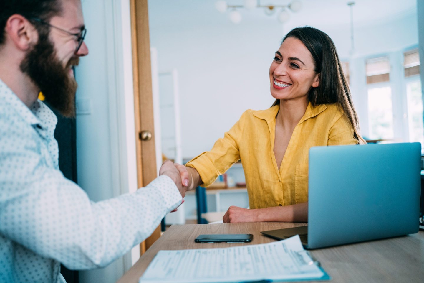 Two workers shaking hands over a laptop