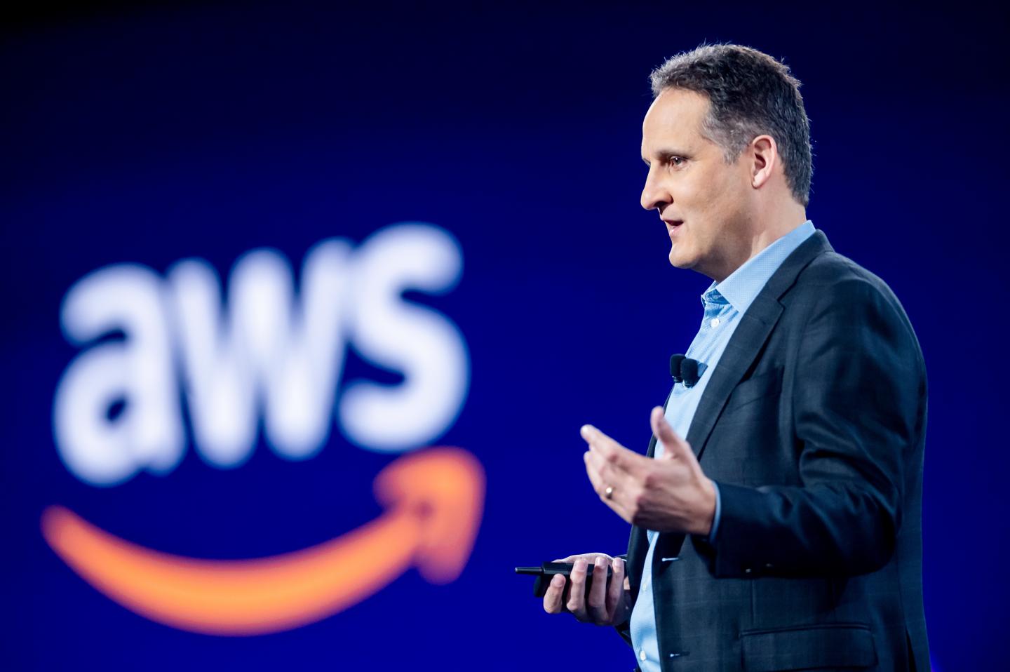 AWS CEO Adam Selipsky delivering a keynote with the letters AWS blurred in the background.