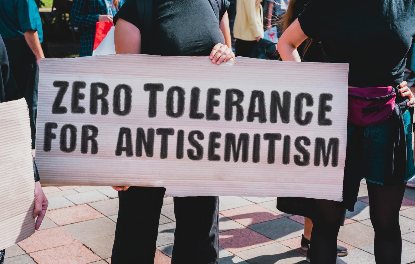 A woman wearing a black t-shirt holding a sign that reads "Zero tolerance for antisemitism"