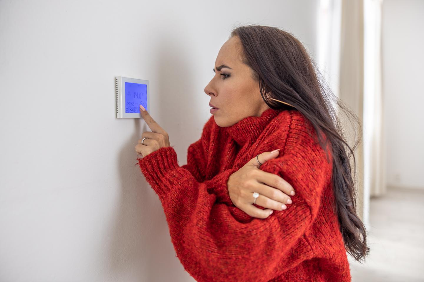 A cold woman adjusts her thermostat.