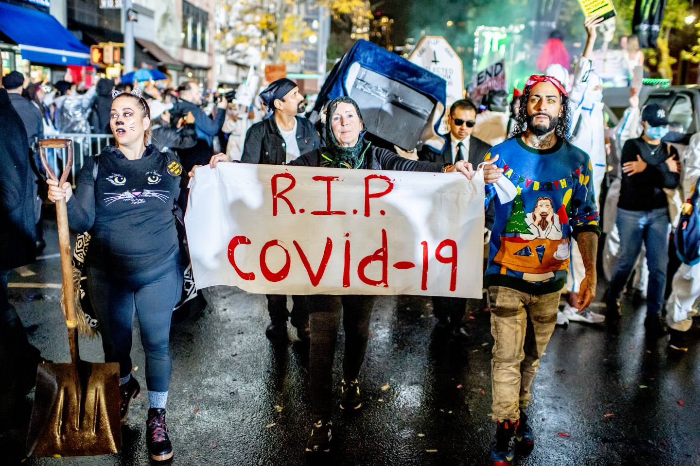 Parade participants in costume holding a sign reading "R.I.P. Covid 19" as they attend the 2022 Halloween Parade on Oct. 31 in New York City.