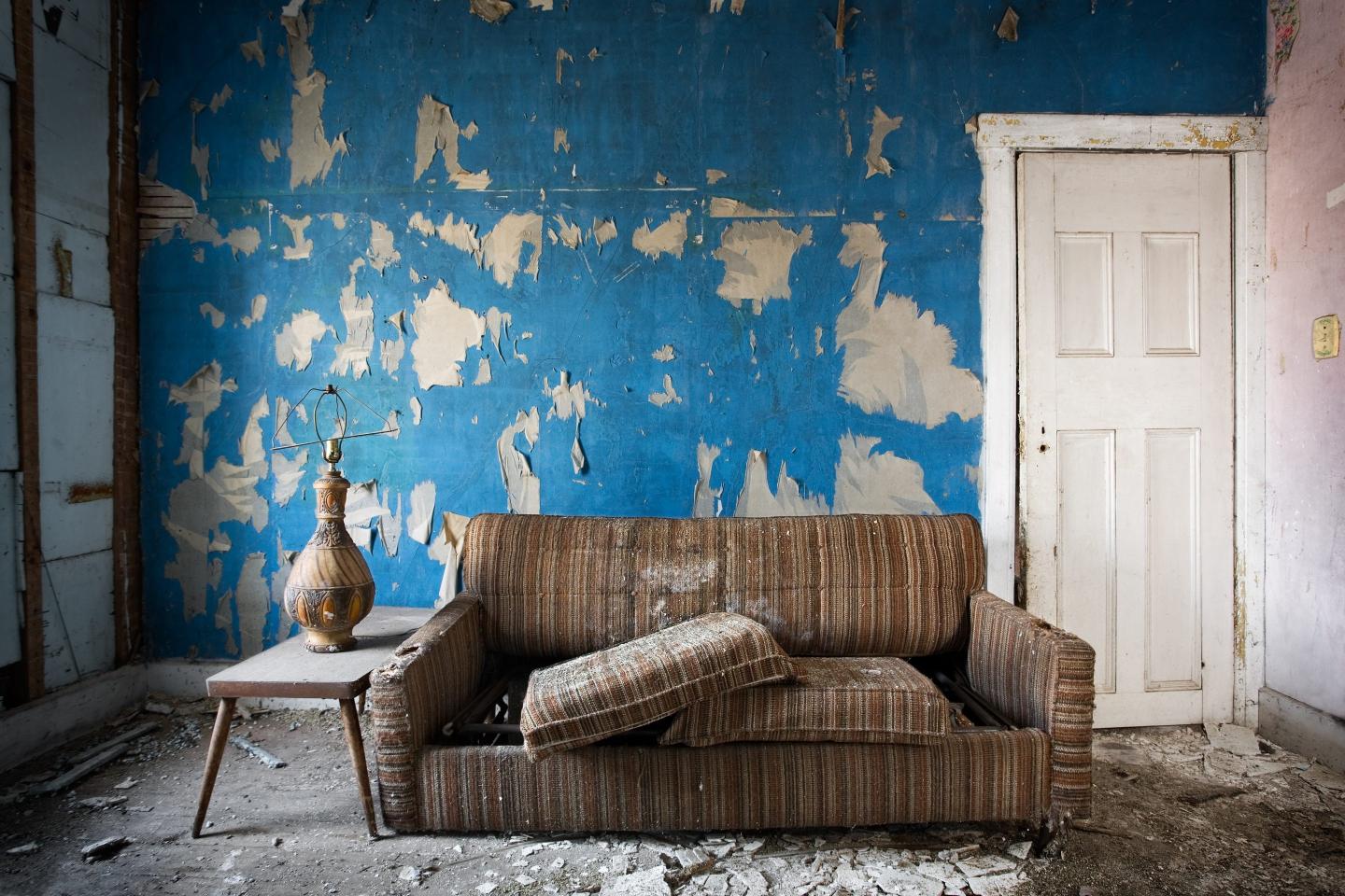 An old couch in front of a peeling wall