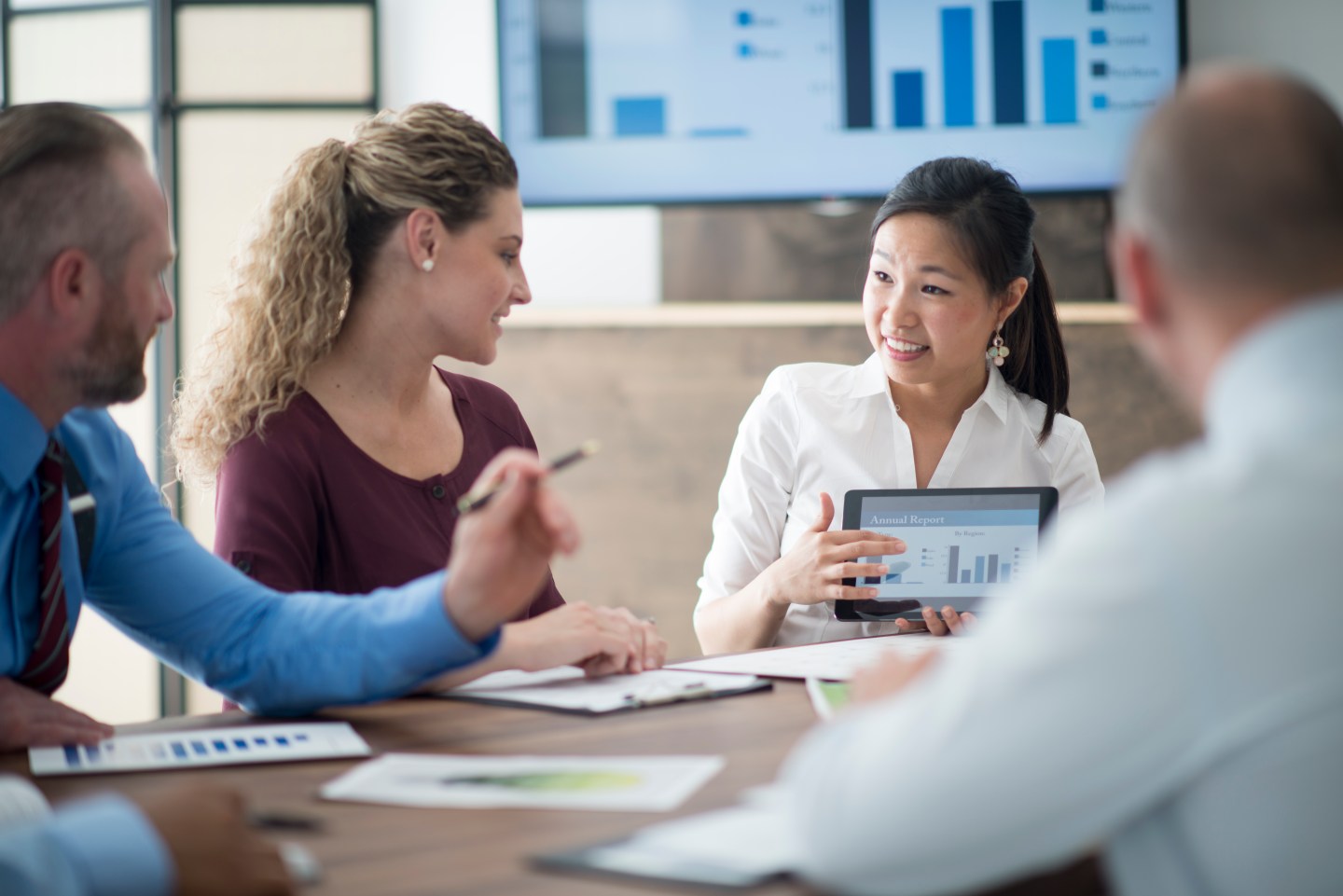 A multi-ethnic group of business associates are in the boardroom and are having a team meeting. They are looking over data, charts, and reports.
