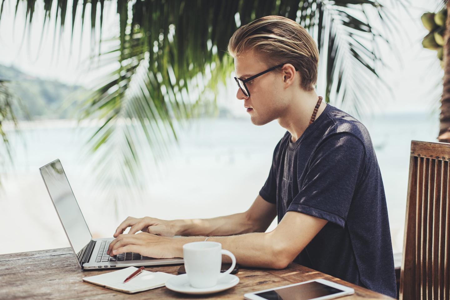 A worker by a tropical beach on laptop