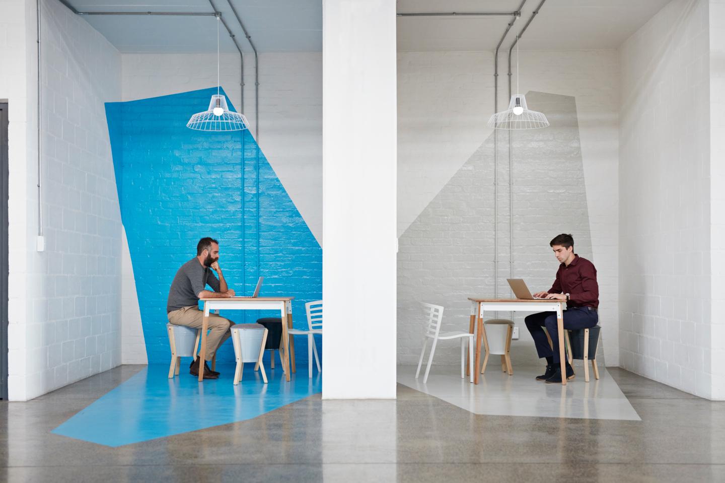 Two people sit on opposite sides of a wall working on their laptops