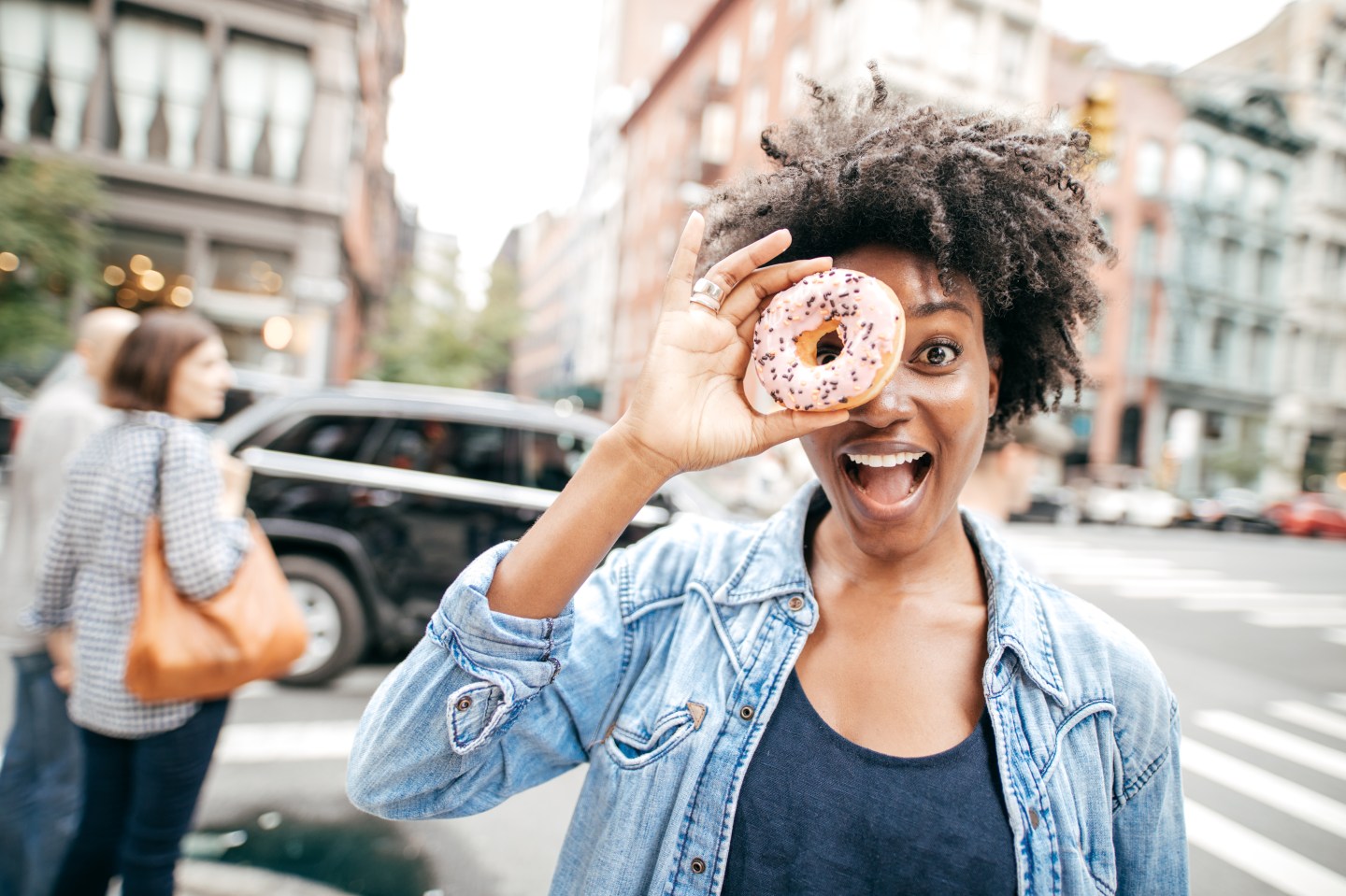 A young woman in a city holding a doughnut up to her eye