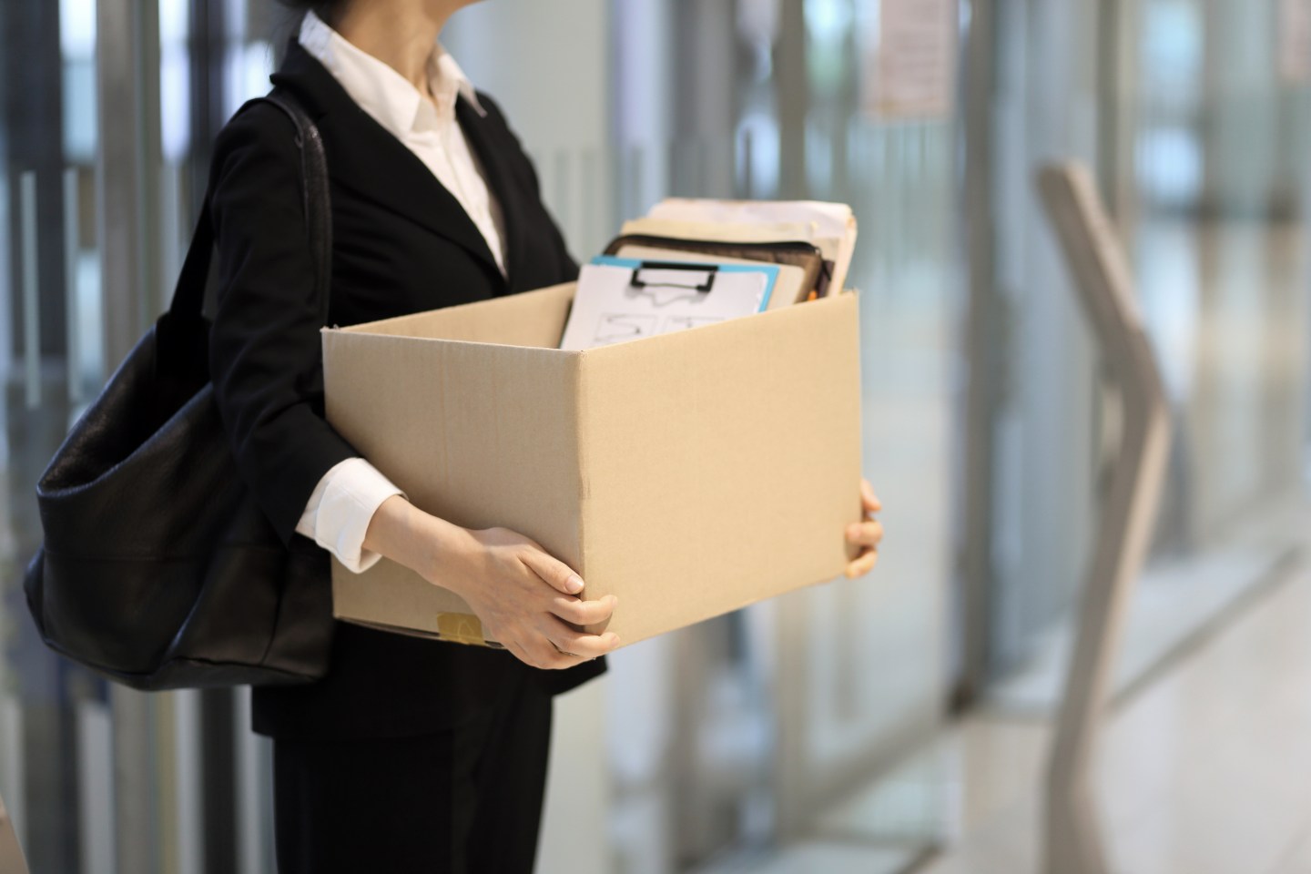 A woman wearing a suit is seen leaving an office carrying her belongings in a cardboard box.