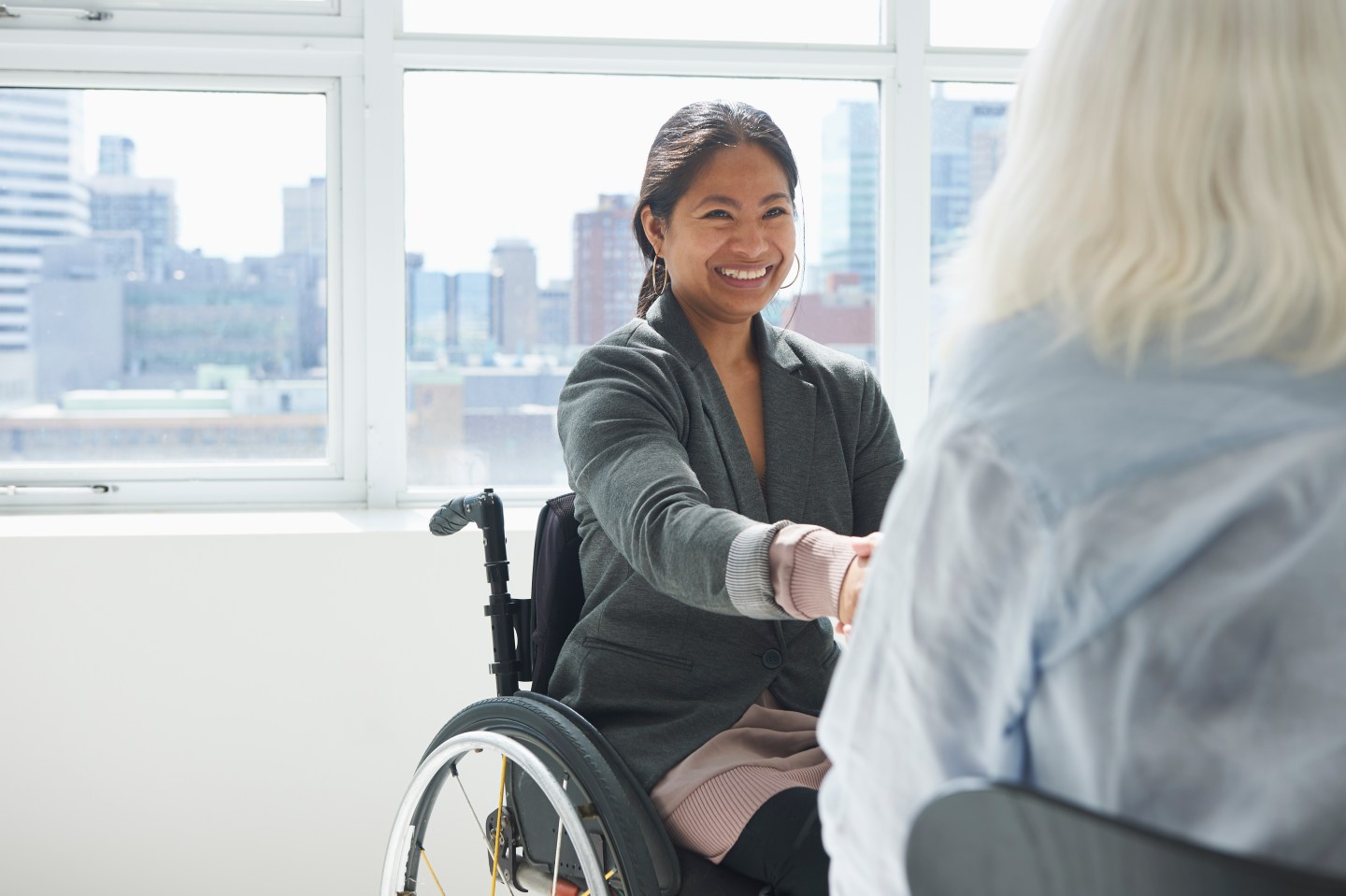 A businesswoman of color in a wheelchair shakes hands with a person across from her.