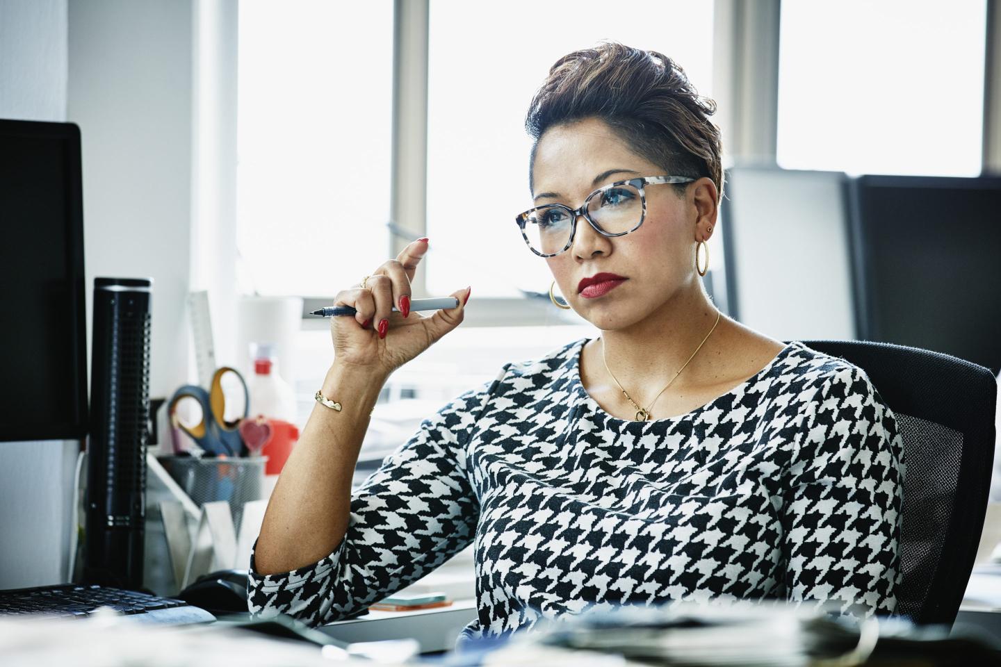 Businesswoman in glasses works at a desk with a serious look on her face