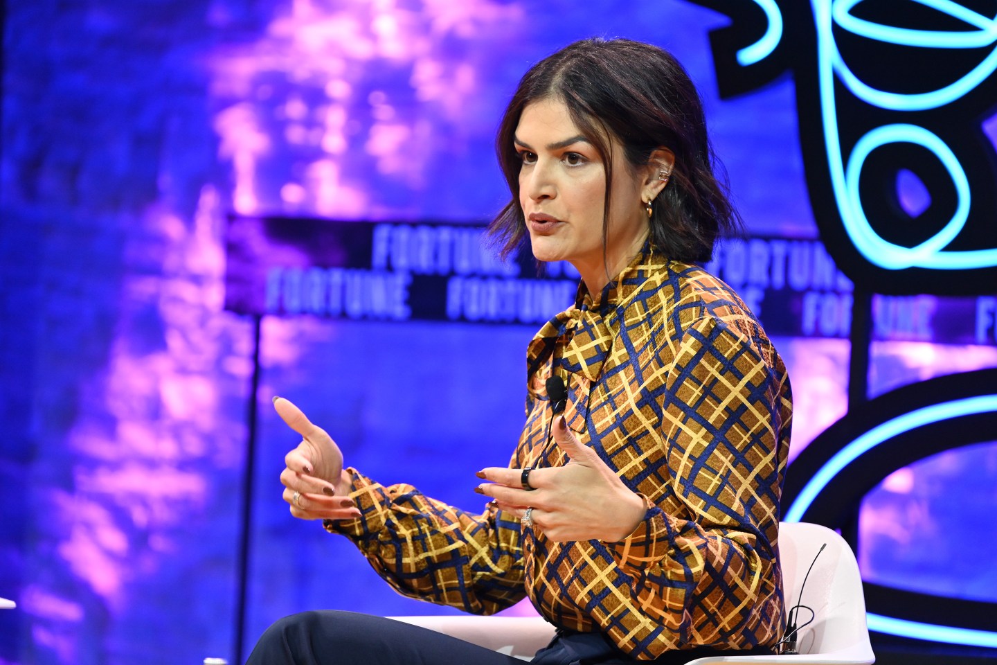 Brunette woman wearing a plaid blouse speaking onstage