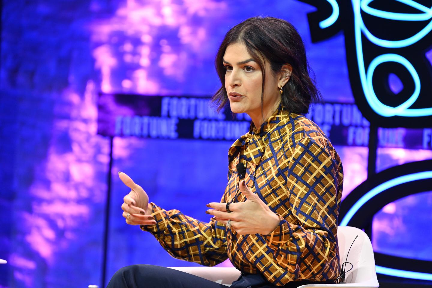 Brunette woman wearing a plaid blouse speaking onstage