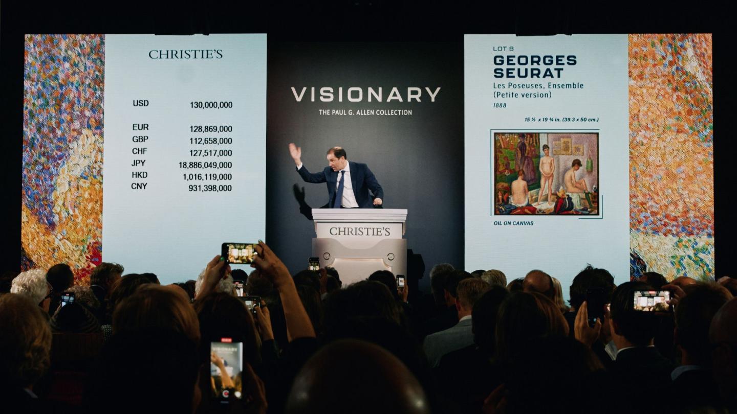 An auctioneer sells Georges Seurat’s Les Poseuses, Ensemble (Petite version) in front of a crowd full of bidders.