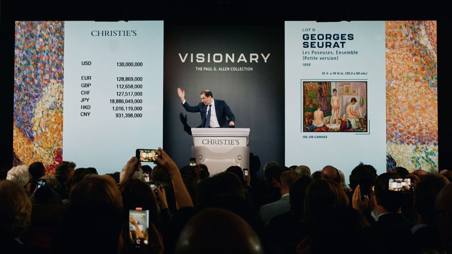 An auctioneer sells Georges Seurat’s Les Poseuses, Ensemble (Petite version) in front of a crowd full of bidders.