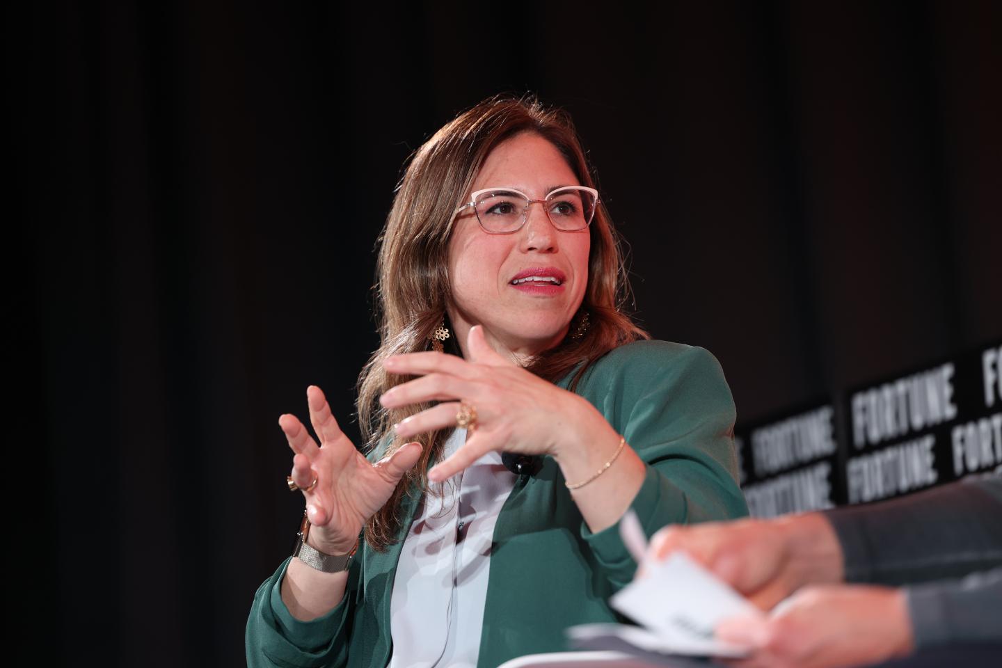 Yael Garten, Director of AI/ML Data Science and Engineering, Apple discussing a topic on stage with her hands up.