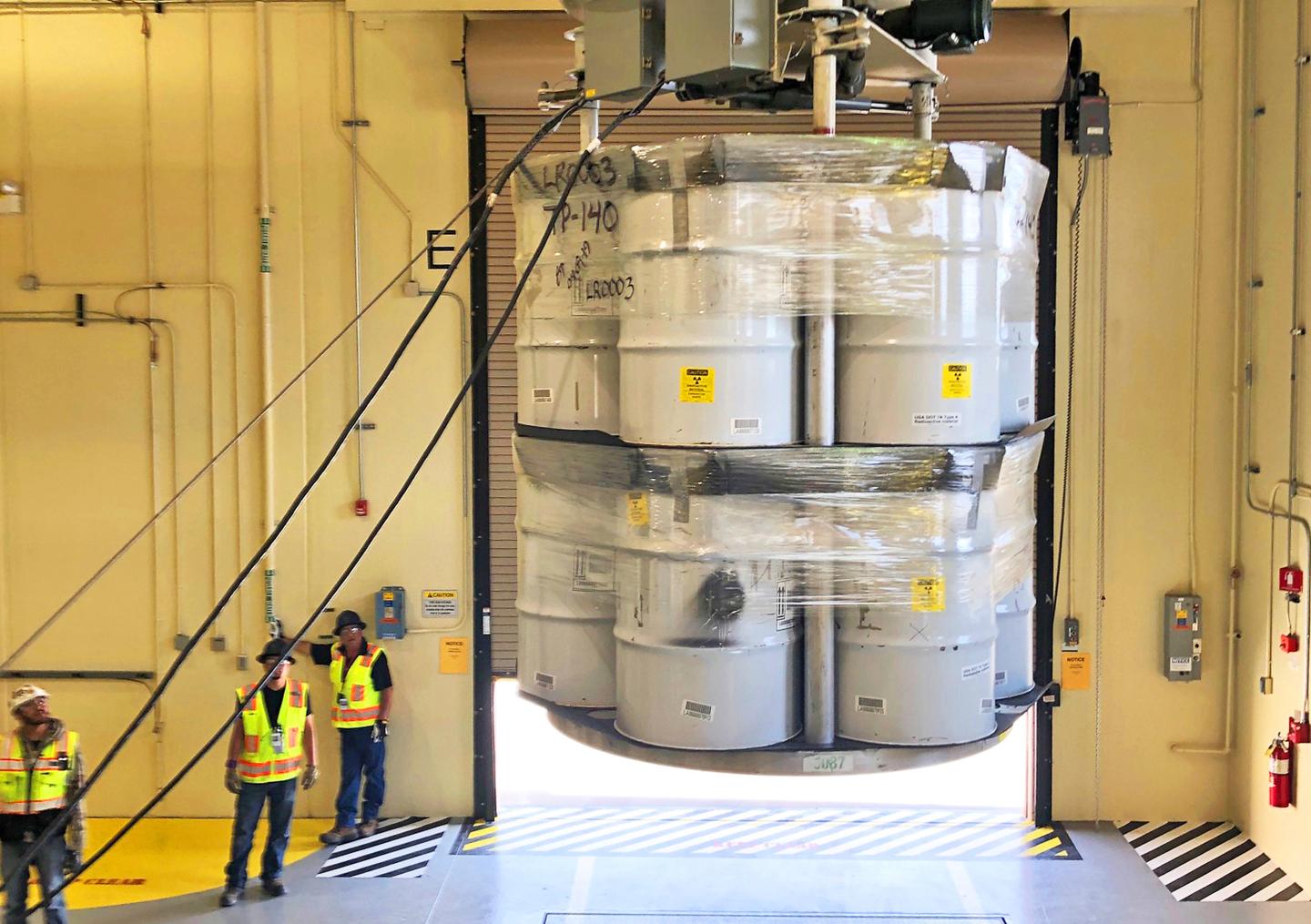 Workers standing next to barrels of radioactive waste.