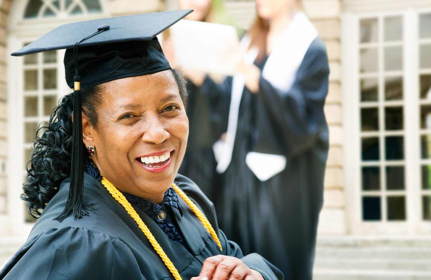 Woman with a graduation cap and gown looks at the camera.