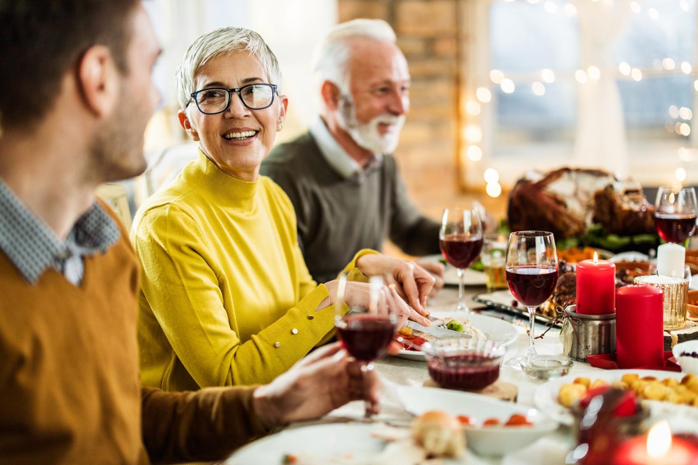 mature woman having a holiday meal with her husband and talking to her adult son at dining table.