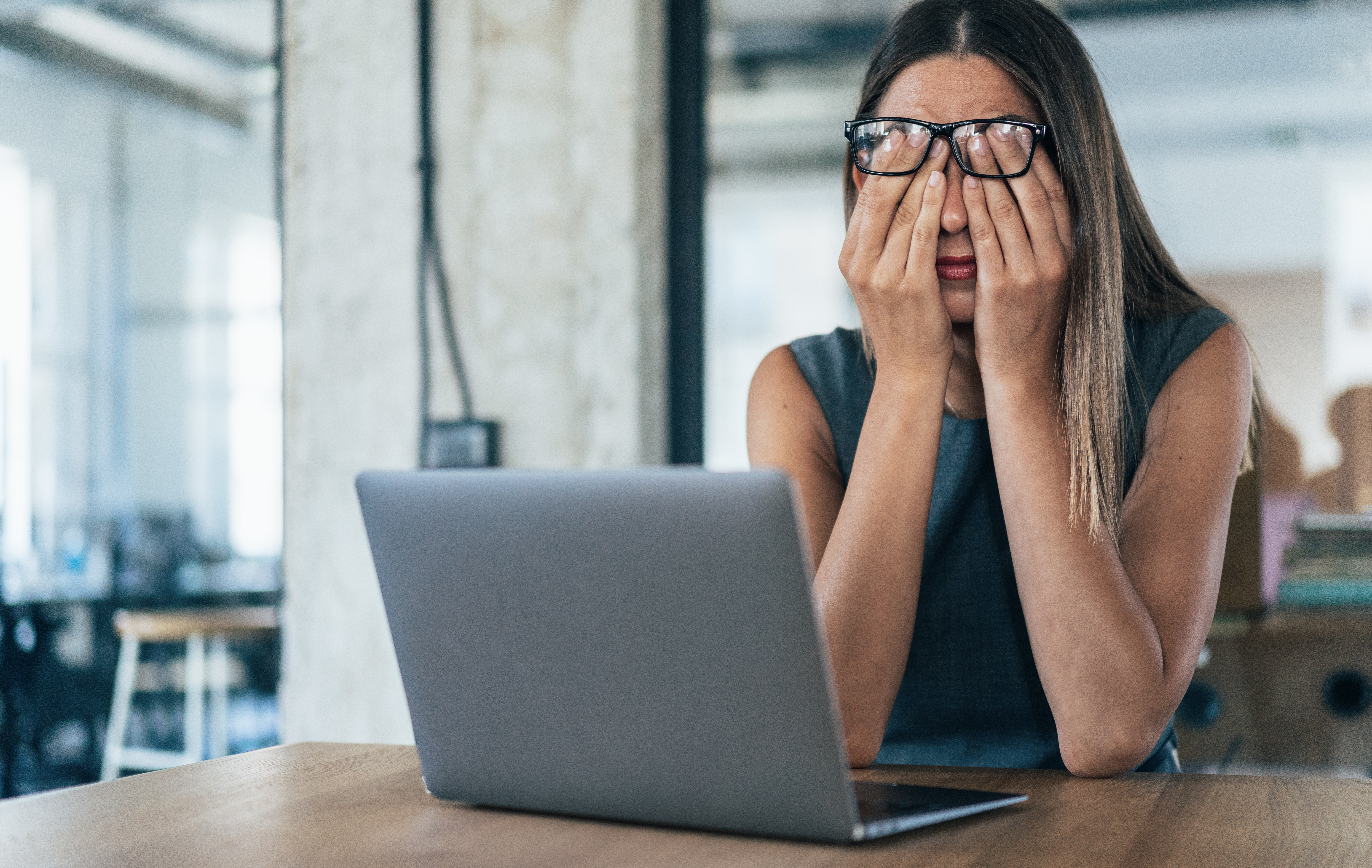 Image of a tired businesswoman rubbing her eyes while working on a laptop