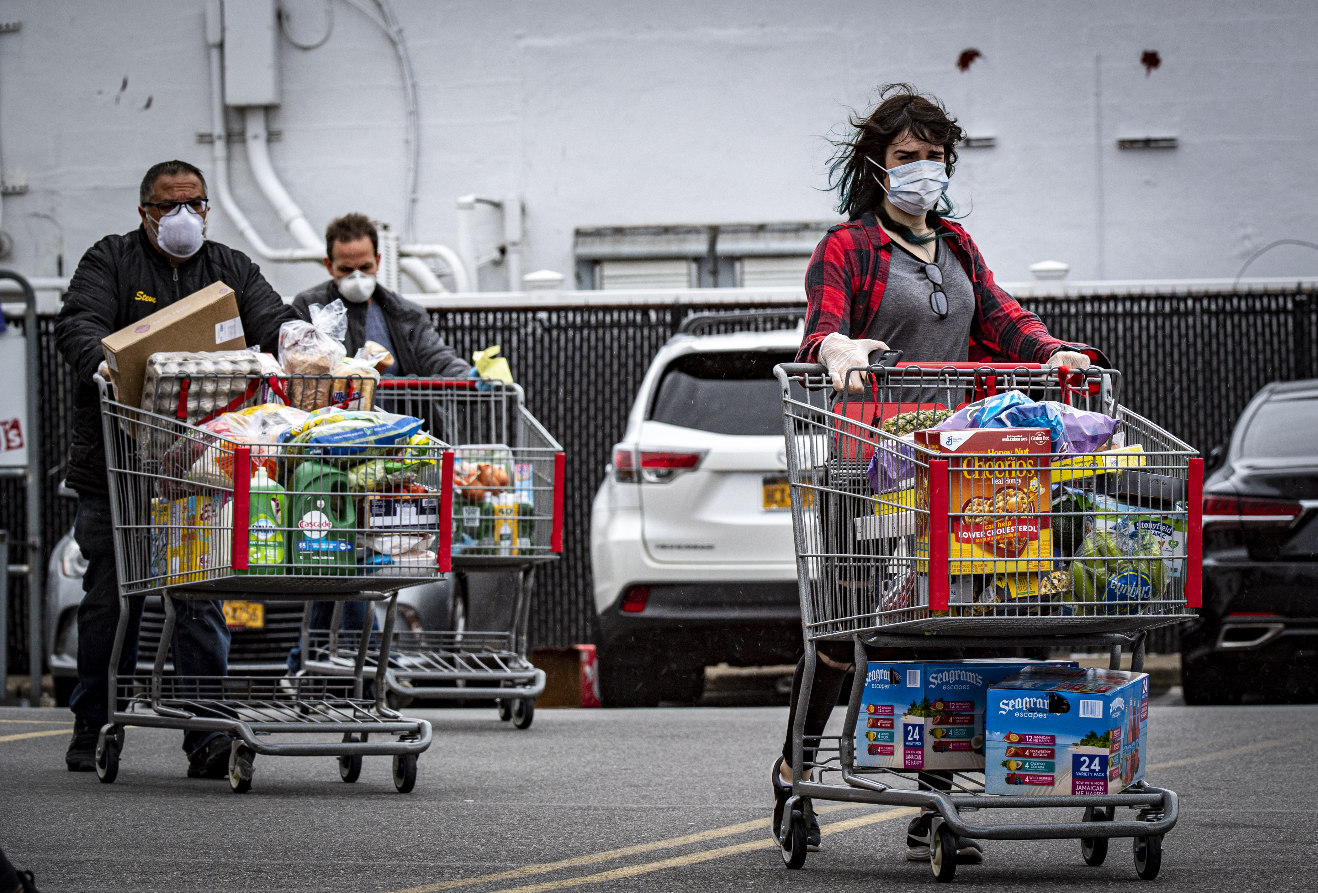 People pushing grocery carts in a parking lot.