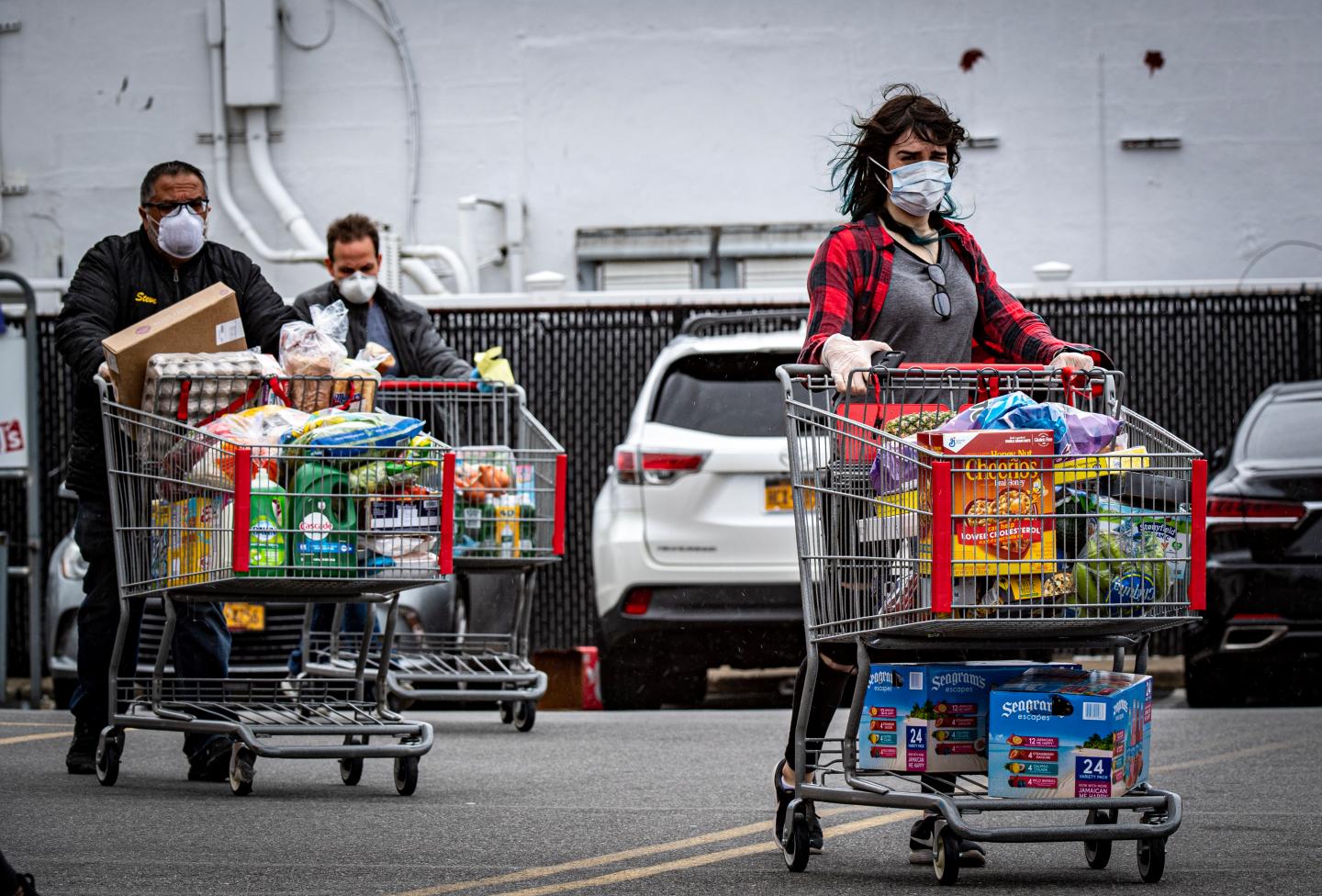 People pushing grocery carts in a parking lot.