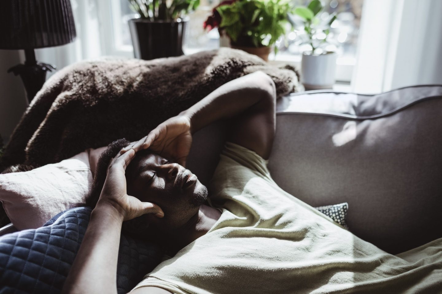 High angle view of Black man with headache lying on sofa at home