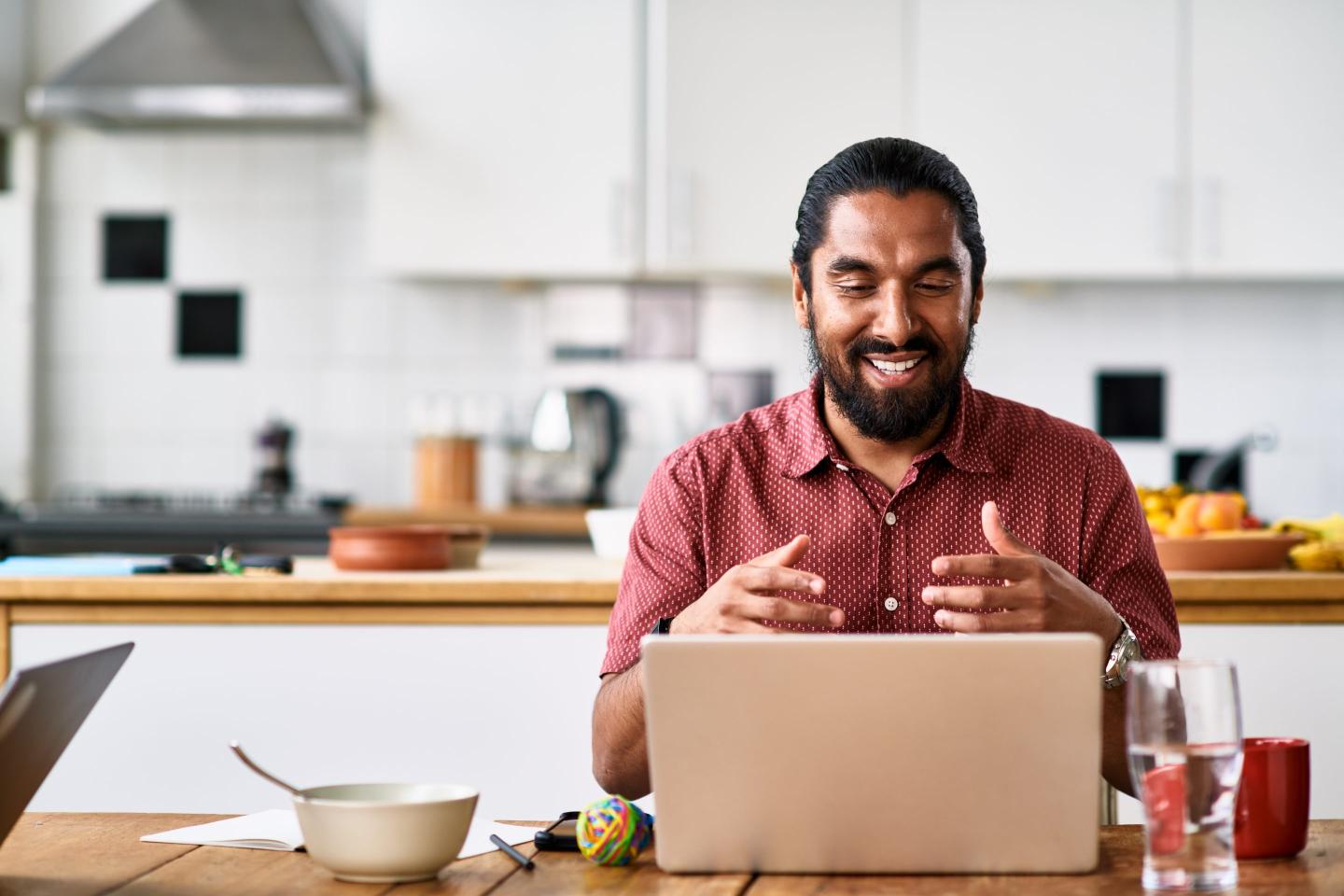 A man in a virtual meeting, on the laptop while in the kitchen