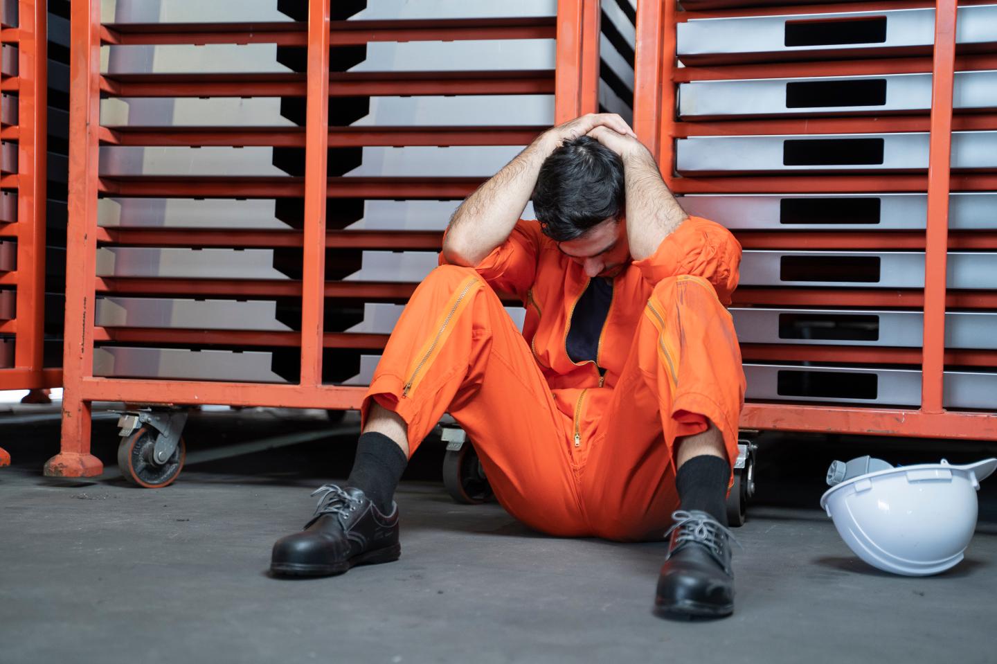 A man sits on the floor with his hands on his head looking sad.