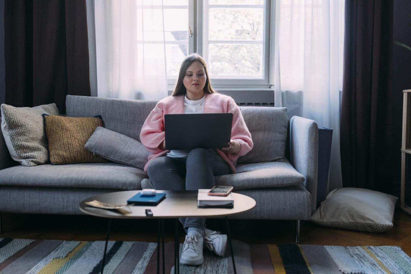 Beautiful Woman Sitting on the Sofa in her Living Room and Browsing the Web on a Laptop