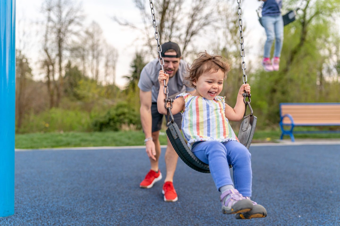 A two-year-old girls laughs while her father pushes her on a swing