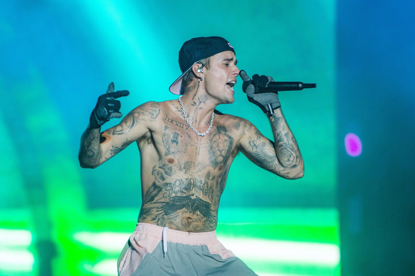 A shirtless Justin Bieber sings into a microphone in front of a green background
