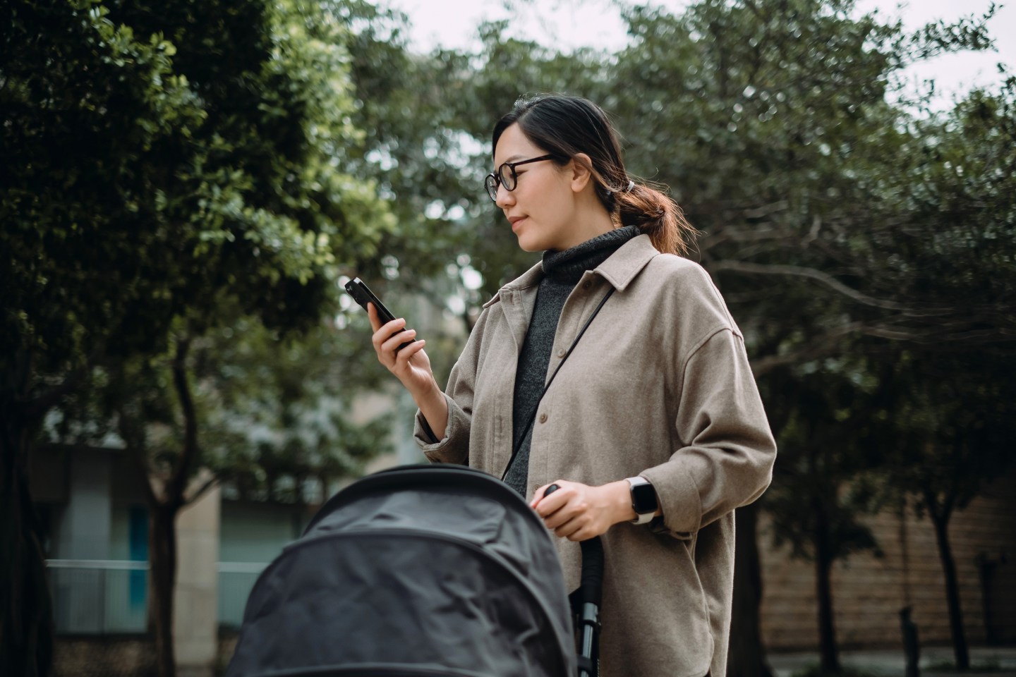 Young Asian mother using smartphone while pushing her little baby in the stroller.