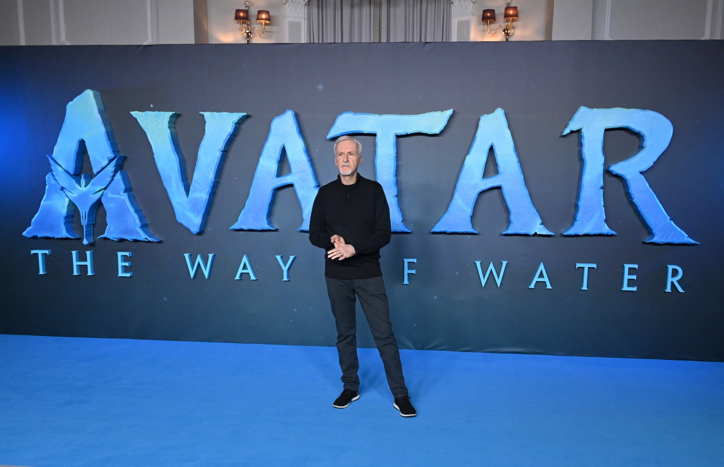 Director James Cameron standing in front of a banner advertising his new film Avatar: The Way of Water at the movie's premiere