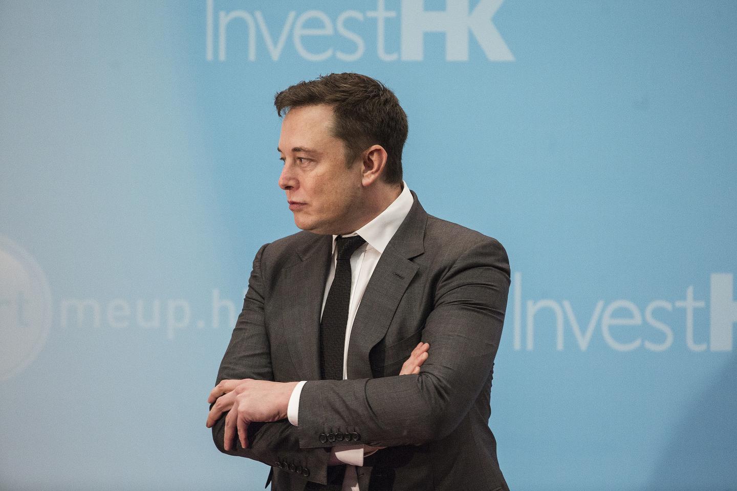 Elon Musk standing on stage with arms crossed