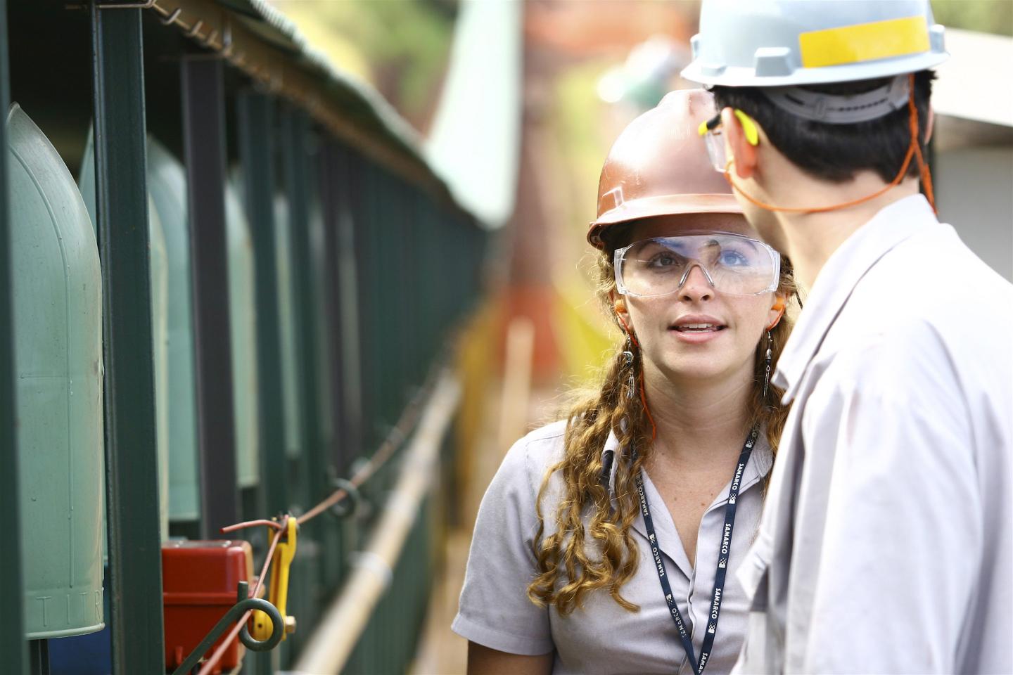 A woman wearing a hard hat and safety goggles converses with a man wearing a hard hat.