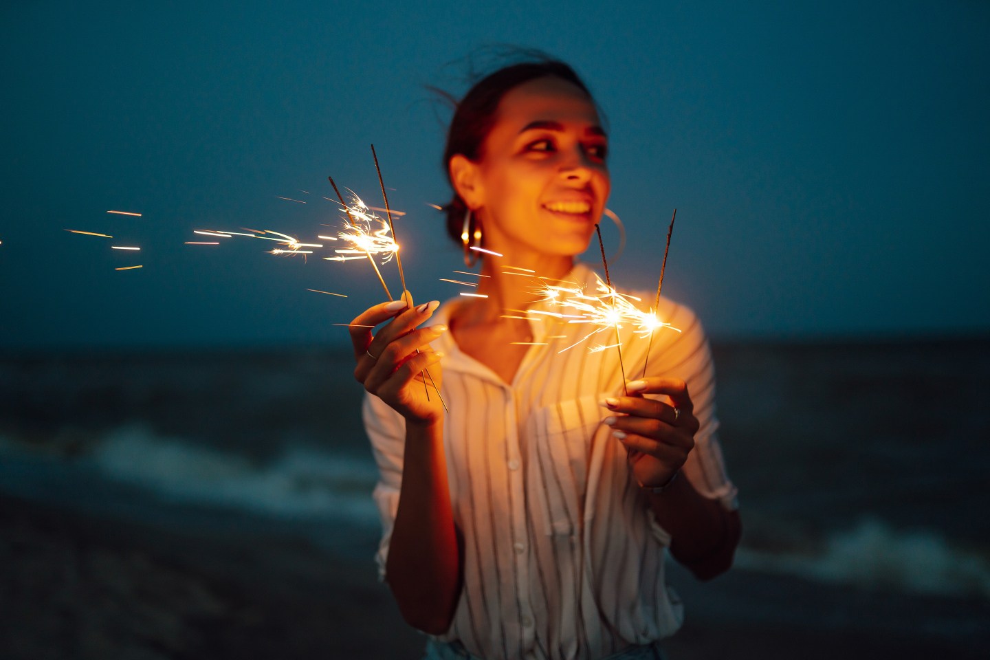 A happy woman smiling and holding sparklers.