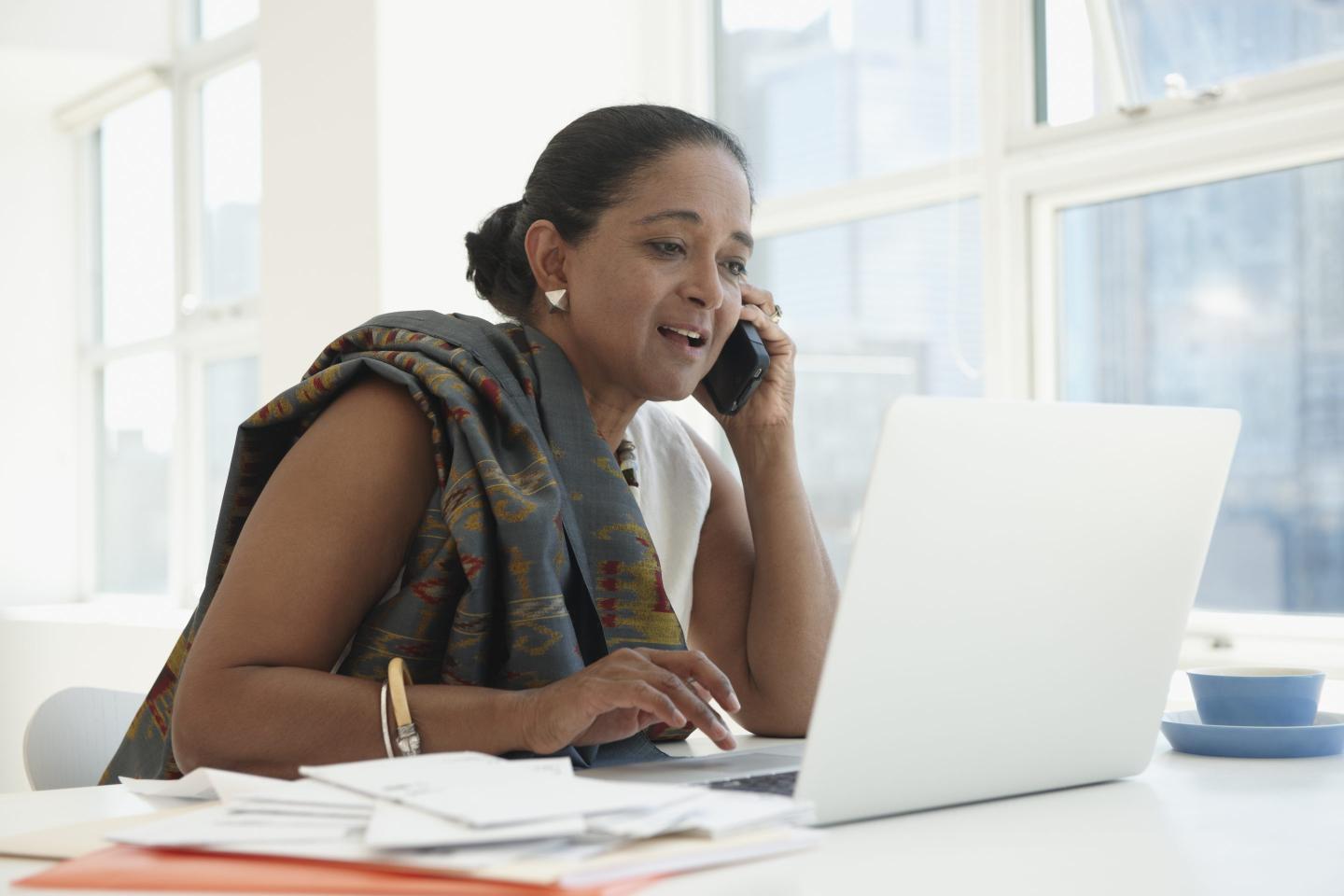 Modern Board - An older indian businesswoman sits behind a laptop